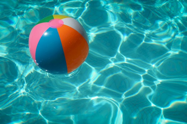 A colorful beach ball floating on the surface of a swimming pool surrounded by clear blue water and sunlight reflections.