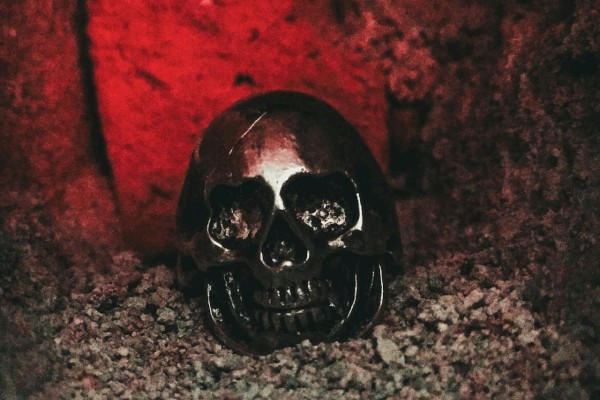 A metallic skull lies on a rough surface with a red-lit background, creating a mysterious and eerie atmosphere.