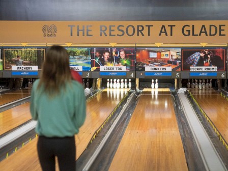 A person is bowling at The Resort at Glade Springs, with various activities like laser tag and escape rooms on display.