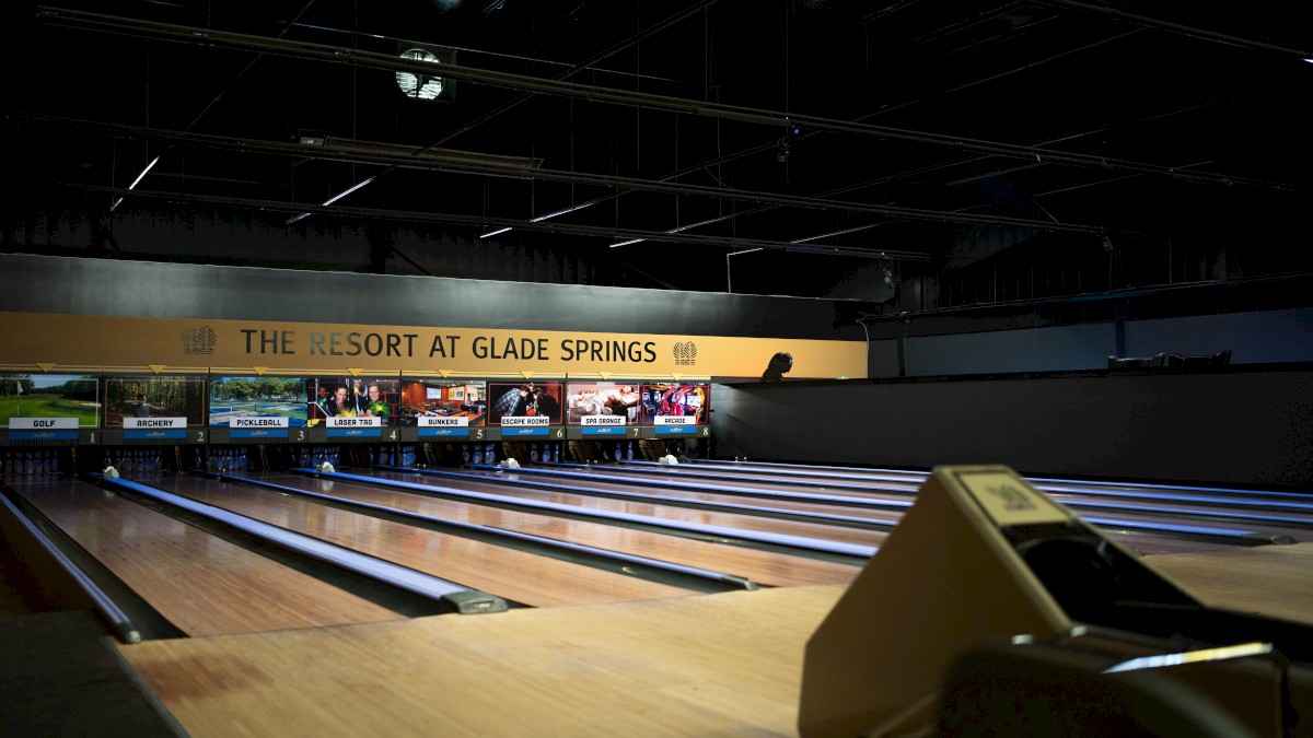 An indoor bowling alley with multiple lanes and screens displaying various game options and prices at Glade Springs Resort.