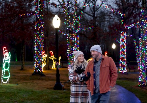 A couple walks through a park decorated with colorful holiday lights on trees and glowing figures, creating a festive atmosphere.