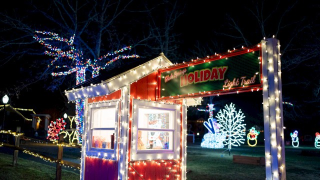 A festive holiday light display featuring a small booth, illuminated trees, and colorful decorations, creating a cheerful atmosphere.