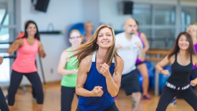 A group of people energetically participating in a dance workout class in a gym setting, all dressed in athletic wear.