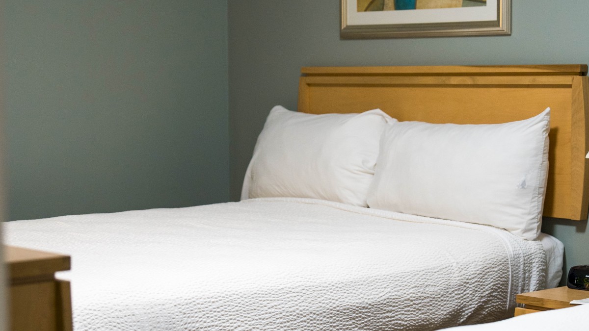 The image shows a hotel room with two neatly made beds, a framed artwork on the wall, and soft lighting, creating a cozy atmosphere.