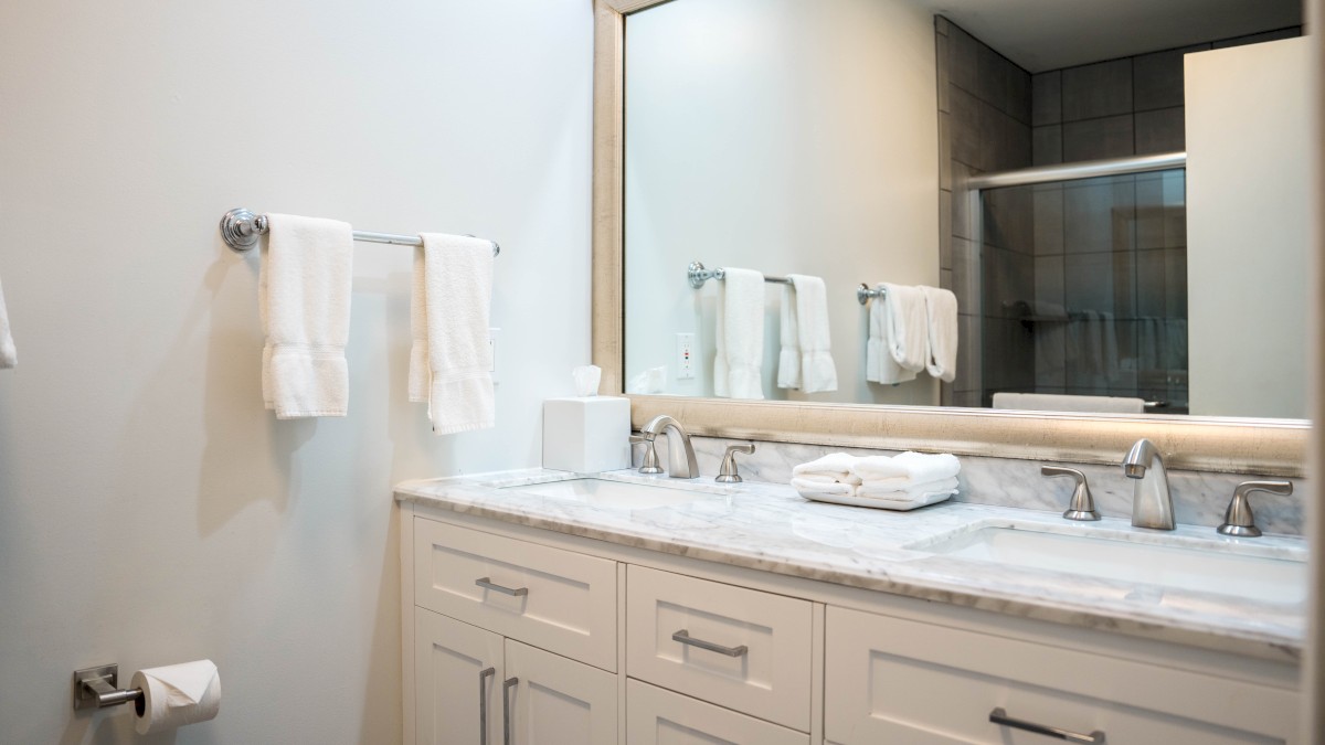 A clean bathroom with a marble countertop, towels, a mirror, and a shower stall in the background.