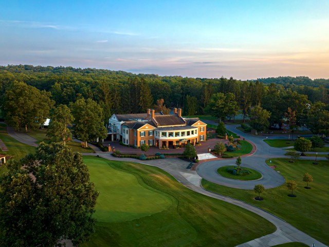 Aerial view of a large building surrounded by greenery and trees, with winding pathways and a lush landscape at sunset.