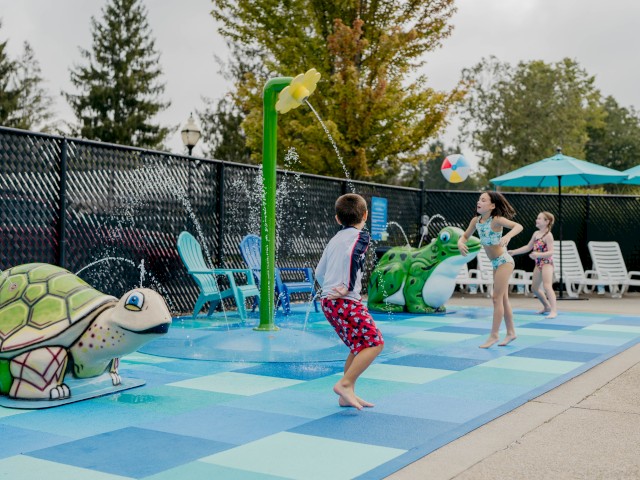 Kids playing in a water splash pad with turtle sculptures and lounge chairs around, enjoying a fun outdoor activity.