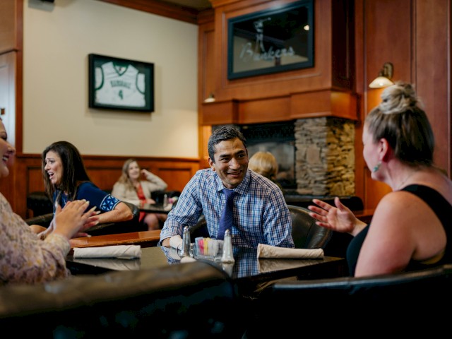People are enjoying a conversation at a restaurant, with framed sports jerseys on the wall and a cozy atmosphere.