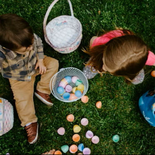 Two children are collecting colorful plastic eggs outdoors for an Easter egg hunt on the grass.