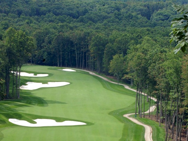A golf course surrounded by dense forest, featuring well-maintained greens and sand bunkers, with a winding path alongside the fairway.