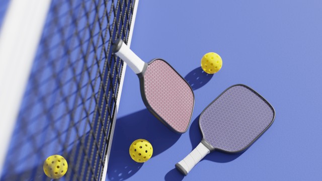 Two pickleball paddles and three yellow balls are on a blue court next to a net.