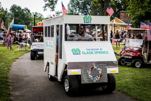A festive parade features decorated golf carts, one labeled 