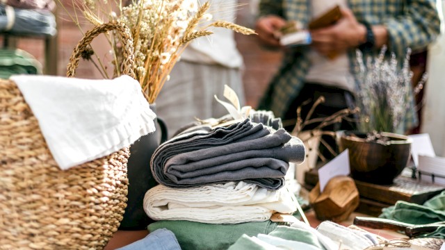 A display featuring folded linens, a basket with dried flowers, and a person in the background holding an item, outdoors.
