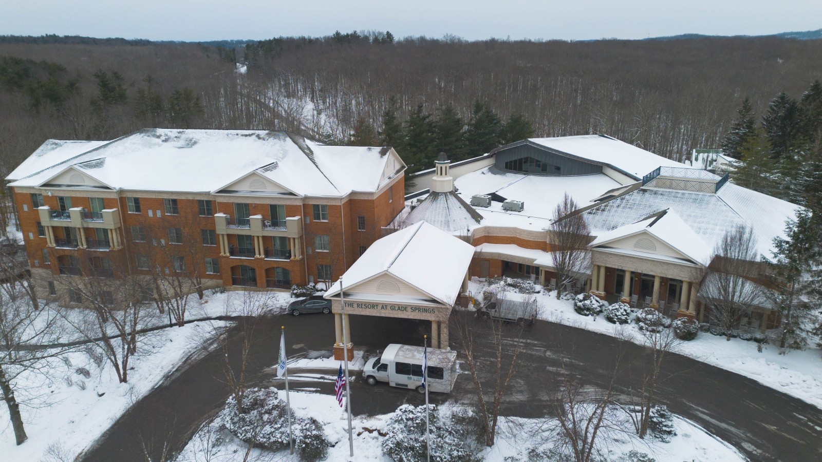 Snowy resort or condo complex with brick buildings, a central covered entrance, a circle driveway, and snow-covered trees surrounding it.