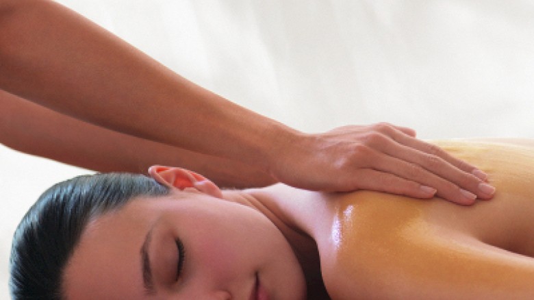 A person lies face down, receiving a back massage from hands on their shoulders, in a calm, relaxing spa-like setting.
