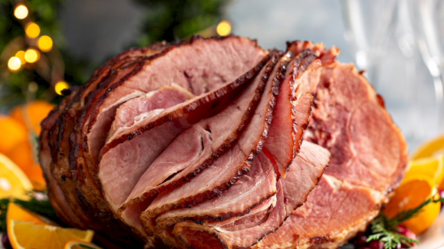 A sliced roasted ham centerpiece on a plate, garnished with orange slices and herbs, festive background lights, flavorful and juicy.