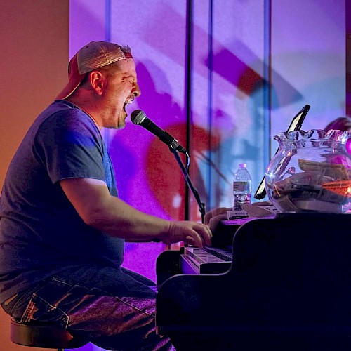 A person is singing and playing a piano on stage, with colorful lights and a microphone.