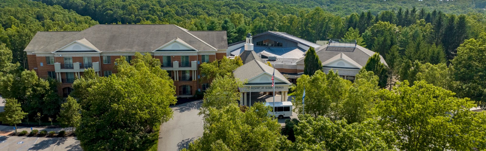 This is an aerial view of a resort surrounded by trees with a parking lot and a bus in front.
