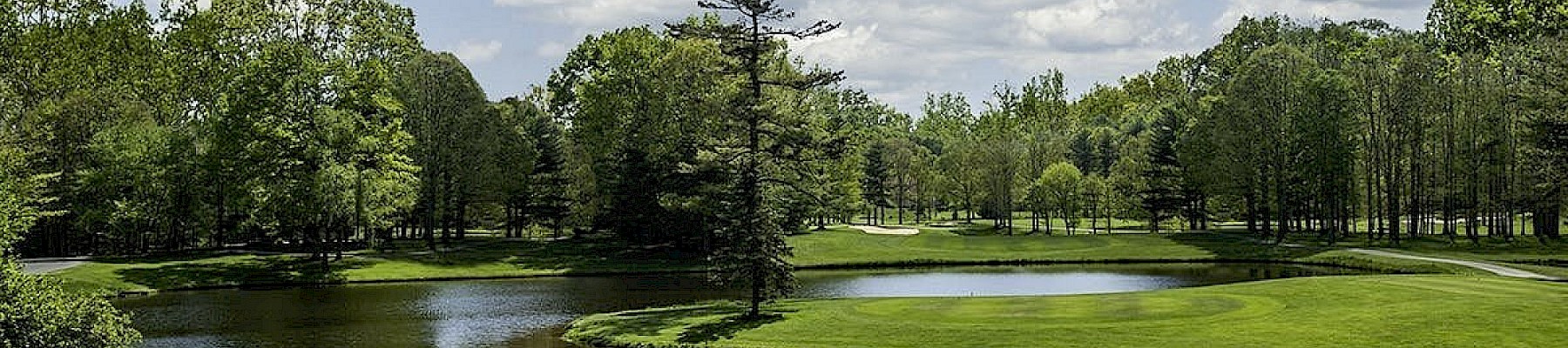 A serene golf course with water features, green trees, and partly cloudy skies in a peaceful outdoor setting.