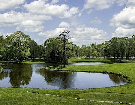 A serene golf course with water features, green trees, and partly cloudy skies in a peaceful outdoor setting.