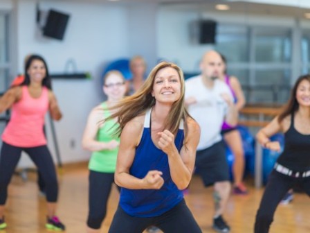 A group of diverse people happily exercising in a fitness class in a bright, modern gym.