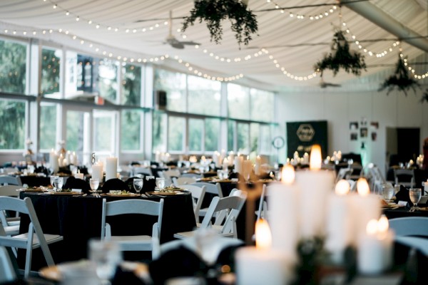 A beautifully decorated event space with tables, candles, and string lights, set up for a celebration or special gathering indoors.