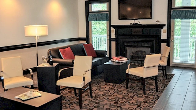 A cozy living room with a black fireplace, TV, white chairs, a sofa with red pillows, and modern decor.