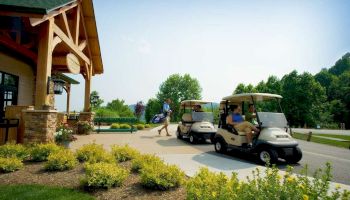 The image shows two golf carts parked near a clubhouse with people in a lush green setting, suggesting a golf course.