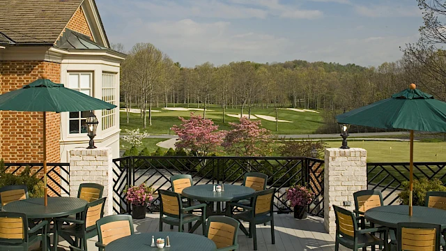 Outdoor patio with tables, chairs, umbrellas, and potted plants overlooking a golf course and blossoming trees.
