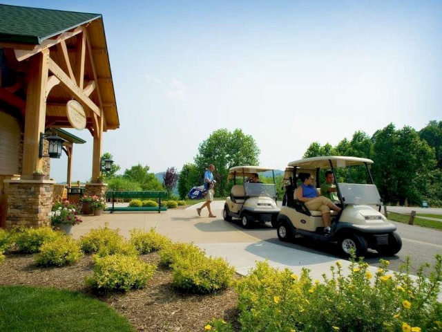 The image shows two golf carts with people near a building surrounded by landscaped greenery and flowers, suggesting a golf course setting.
