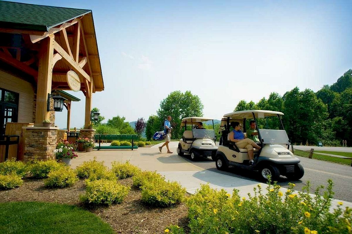 People are using golf carts outside a clubhouse surrounded by greenery and landscaping.