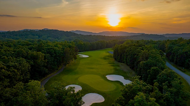 A beautiful aerial view of a golf course at sunset, surrounded by lush trees and rolling hills.