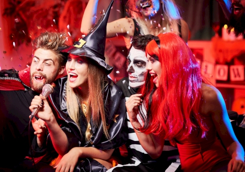 A group of friends dressed in Halloween costumes having fun, singing, and celebrating with confetti and balloons.
