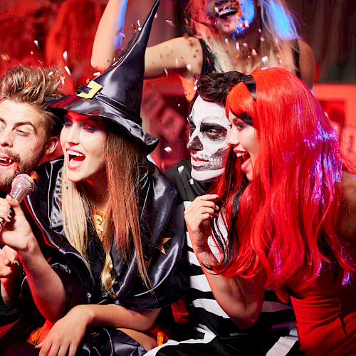 A group of friends dressed in Halloween costumes having fun, singing, and celebrating with confetti and balloons.