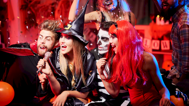 A group of friends dressed in Halloween costumes having fun, singing, and celebrating with confetti and balloons.