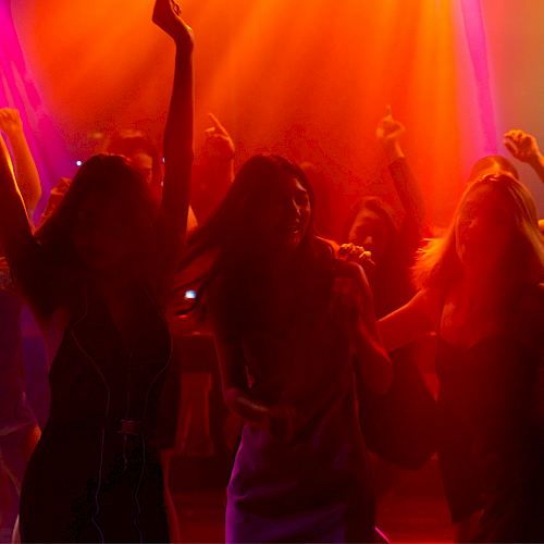 People dancing and having fun at a colorful nightclub with vibrant red, orange, yellow, and purple lighting.