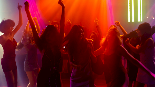 People dancing and having fun at a colorful nightclub with vibrant red, orange, yellow, and purple lighting.