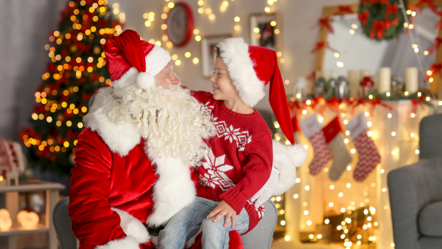 A child and Santa Claus share a joyful moment with Christmas decorations in the background.