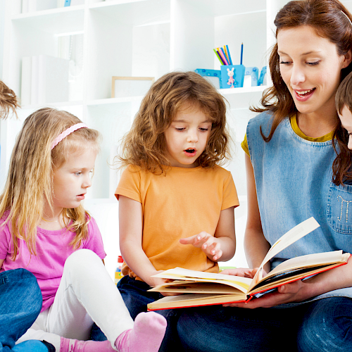A teacher reads a storybook aloud to five children sitting on the floor in a bright, colorful classroom.